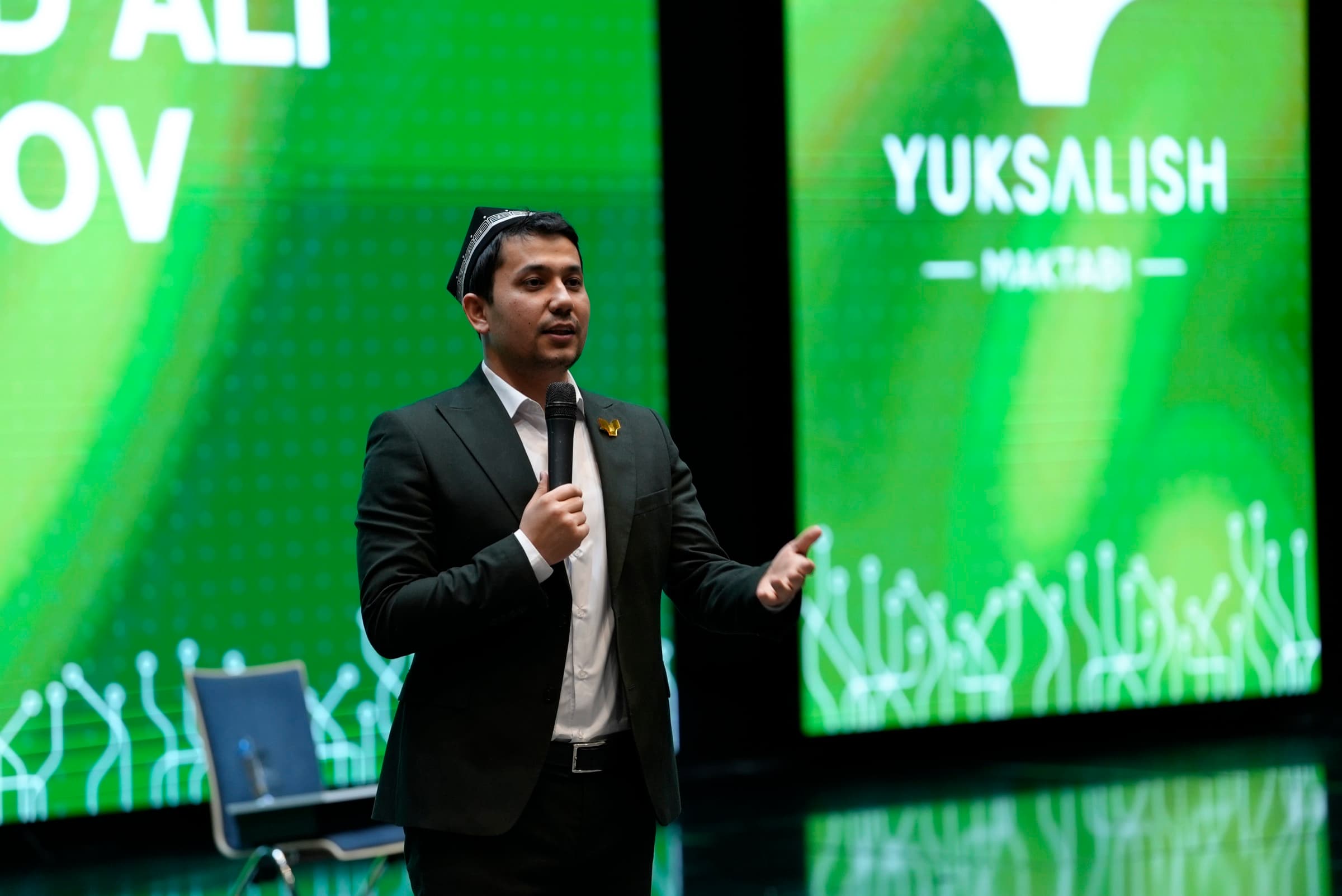 Ma’ruzachi forum sahnasida, orqada yashil LED ekranlar